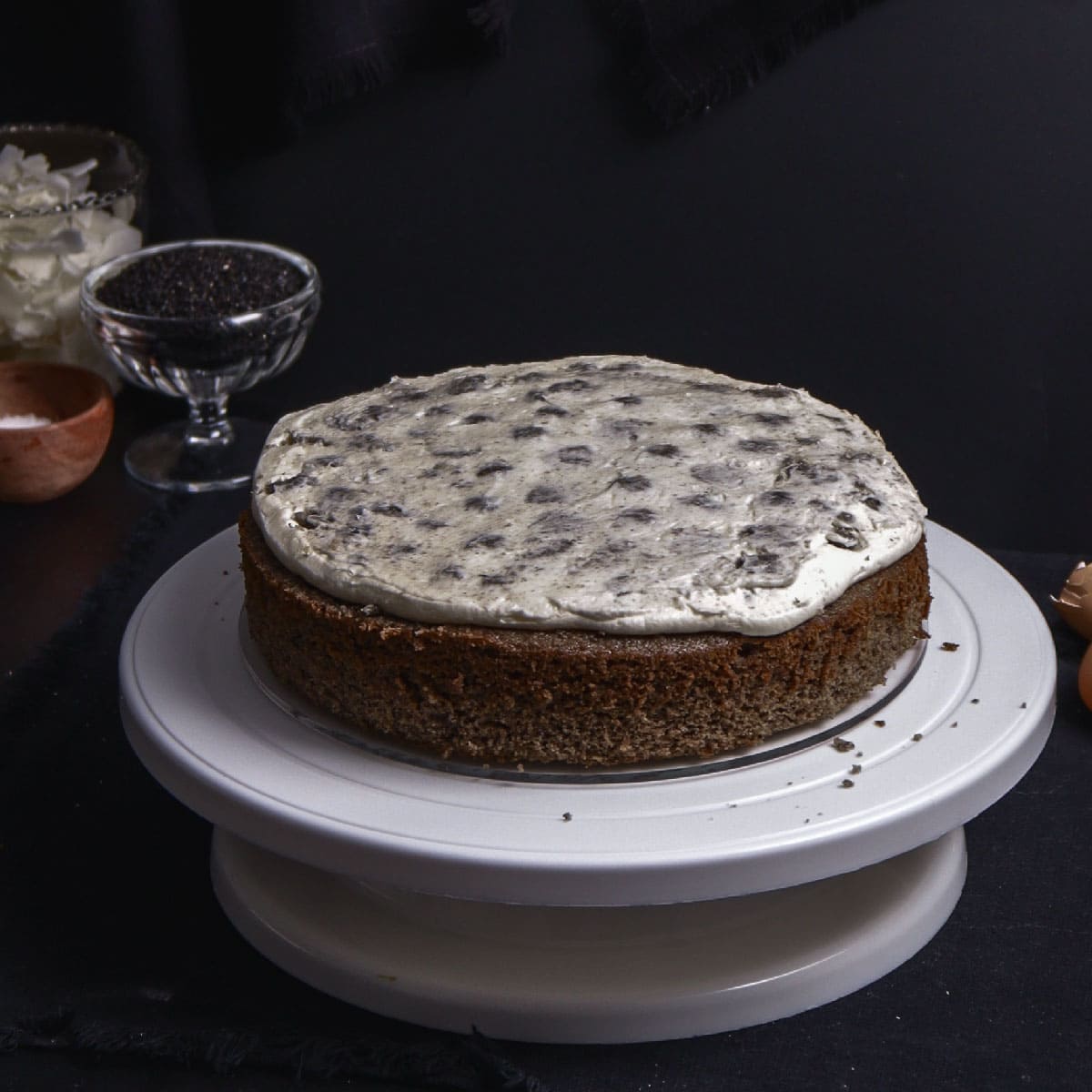 first layer of black sesame cake with coconut buttercream on top with cookie crumbles pushed into the buttercream