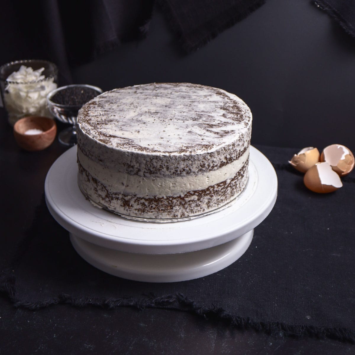 black sesame cake with a crumb coat layer on a white turntable stand