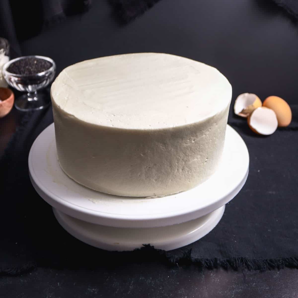 round layer cake covered in white frosting on white turntable