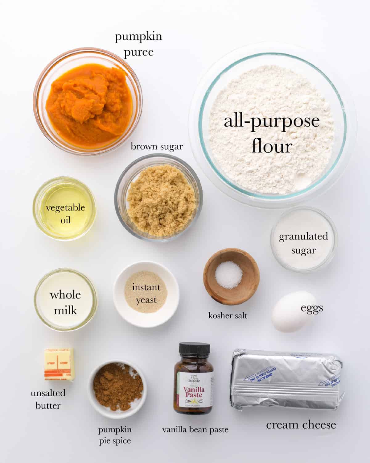overhead view of ingredients, top to bottom: pumpkin puree, all-purpose flour, brown sugar, vegetable oil, whole milk, instant yeast, kosher salt, granulated sugar, eggs, unsalted butter, pumpkin pie spice, vanilla bean paste, cream cheese