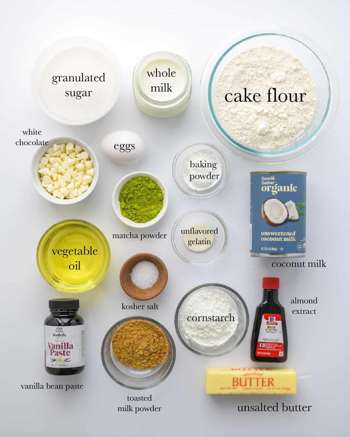 overhead view of ingredients, top to bottom: granulated sugar, whole milk, cake flour, white chocolate, eggs, baking powder, matcha powder, unflavored gelatin, coconut milk, vegetable oil, kosher salt, cornstarch, almond extract, vanilla bean paste, toasted milk powder, unsalted butter