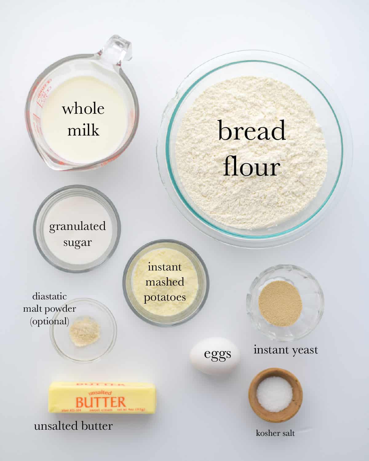 overhead view of ingredients, top to bottom: whole milk, bread flour, granulated sugar, instant mashed potatoes, instant yeast, diastatic malt powder, eggs, unsalted butter, kosher salt