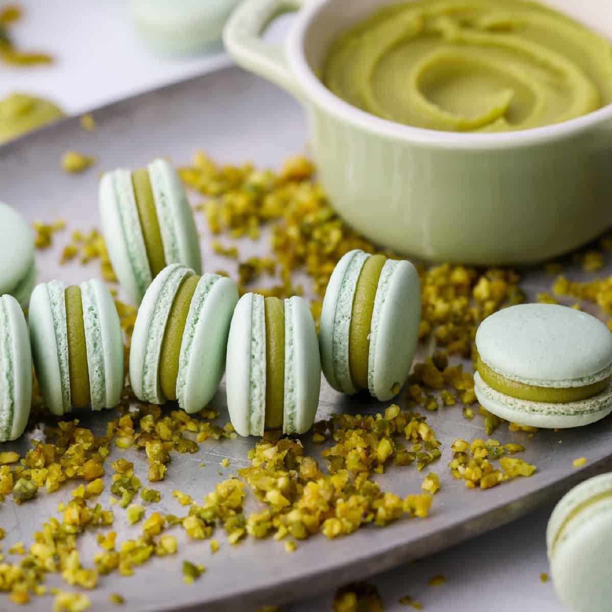pistachio macarons with pistachio filling on a silver tray with ground pistachios nearby.