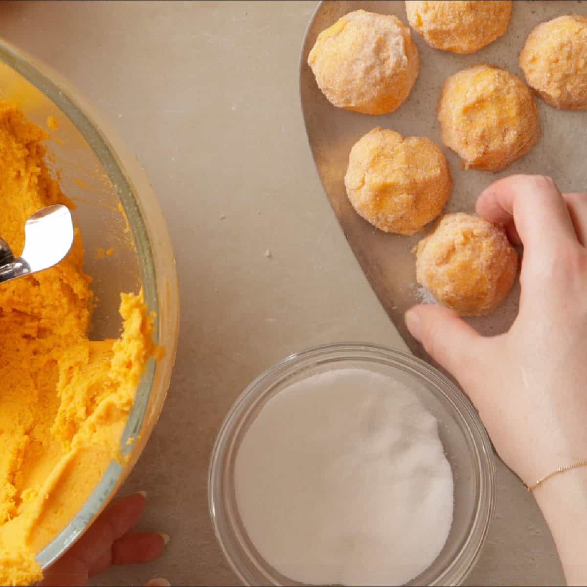 rolling orange cookie dough balls in granulated sugar.